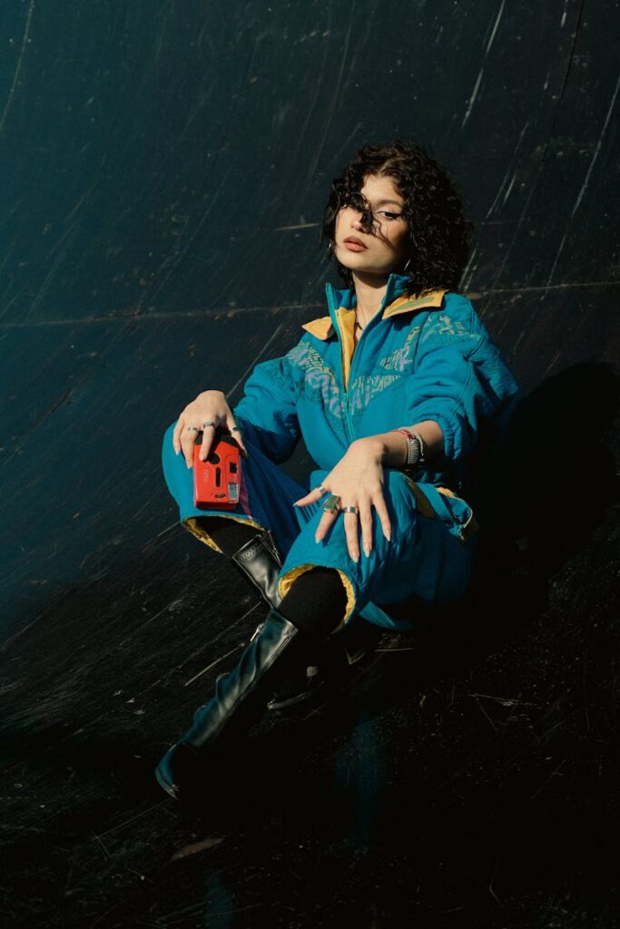 Fashionable woman poses in a vintage jumpsuit with a retro camera against a dark background.