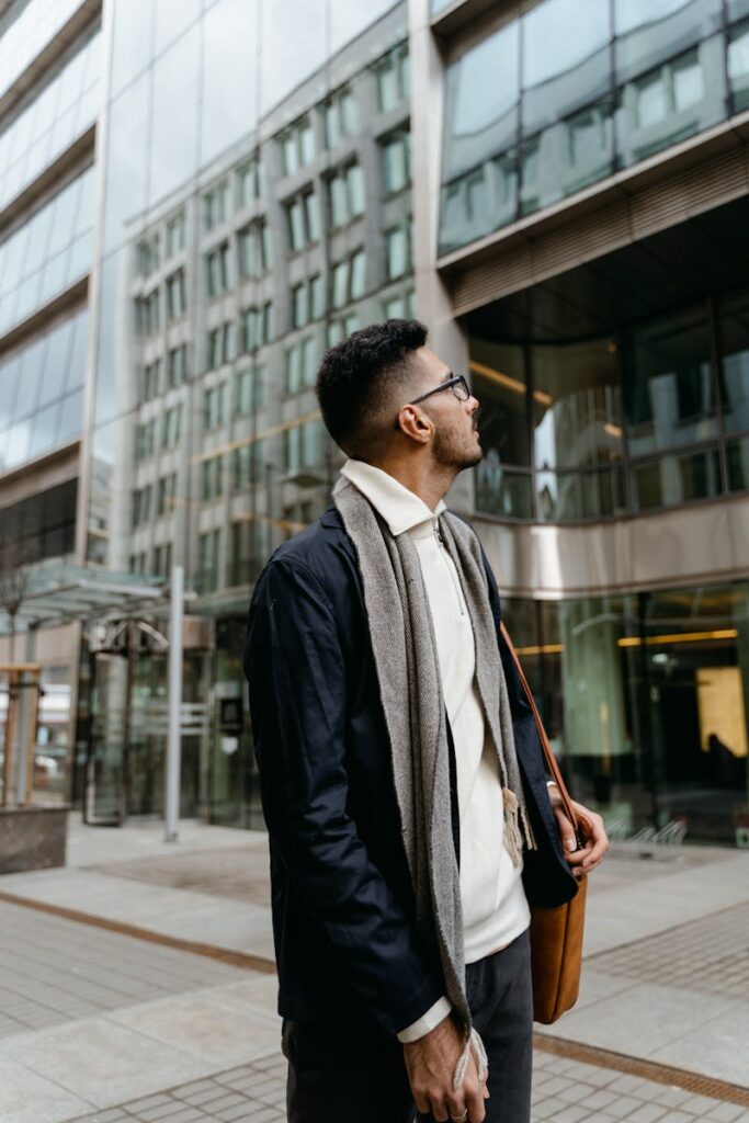 Young businessman in stylish attire outside modern glass office building.