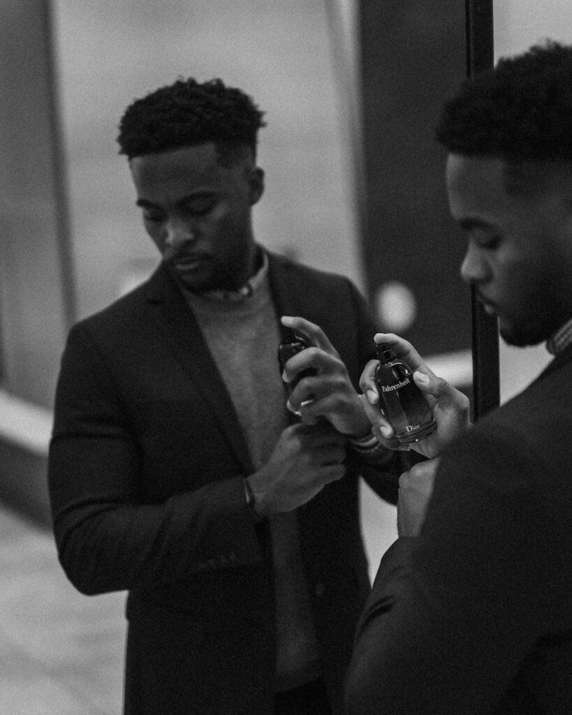 Black and white portrait of a man holding perfume in front of a mirror.