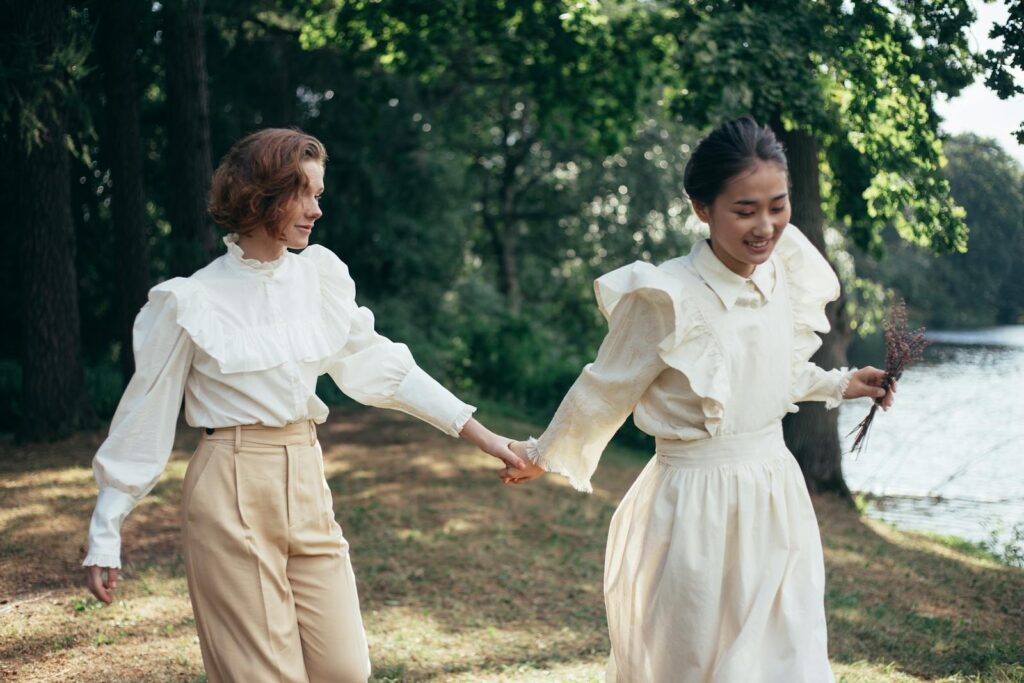 Two women holding hands and smiling while walking in a scenic park.