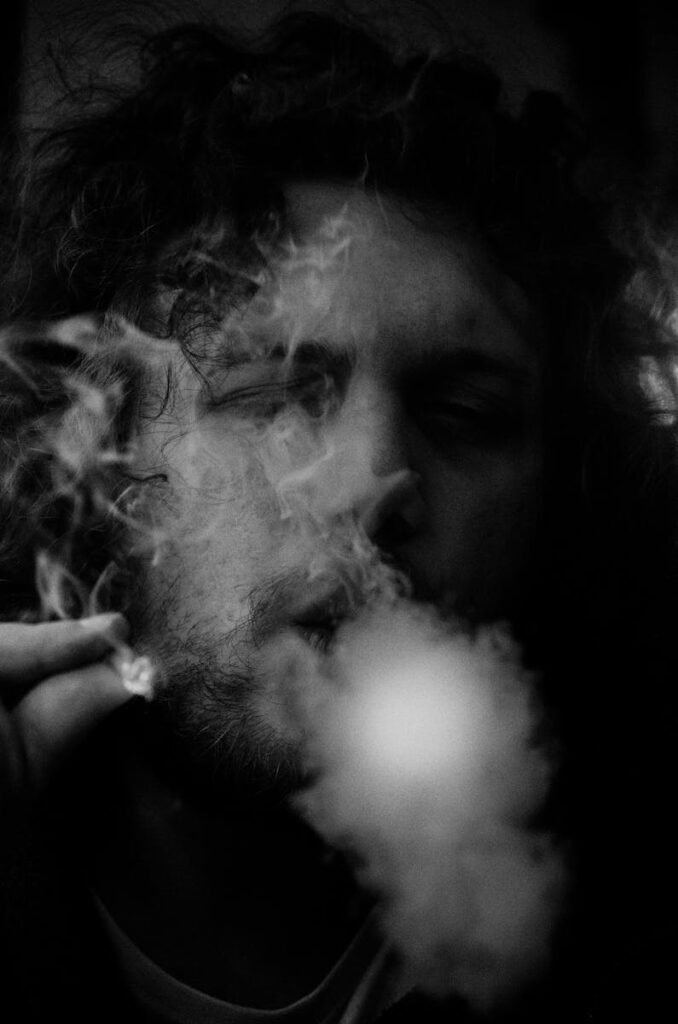Dramatic black and white image of a man exhaling smoke, with rich textures and deep shadows.