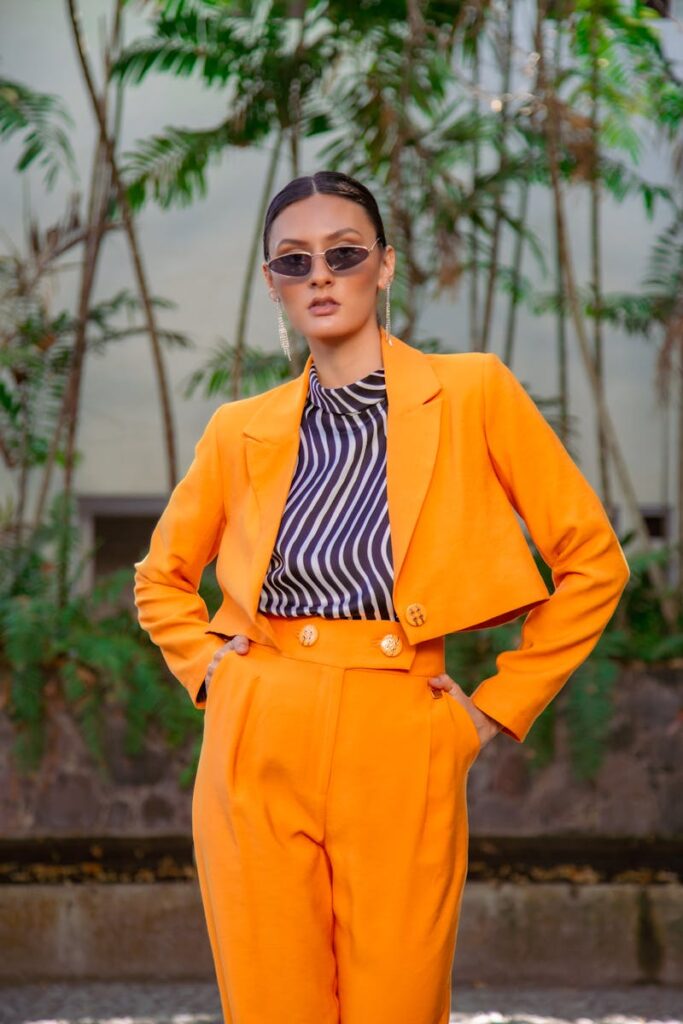 Stylish woman in an orange outfit posing outdoors against a palm backdrop.