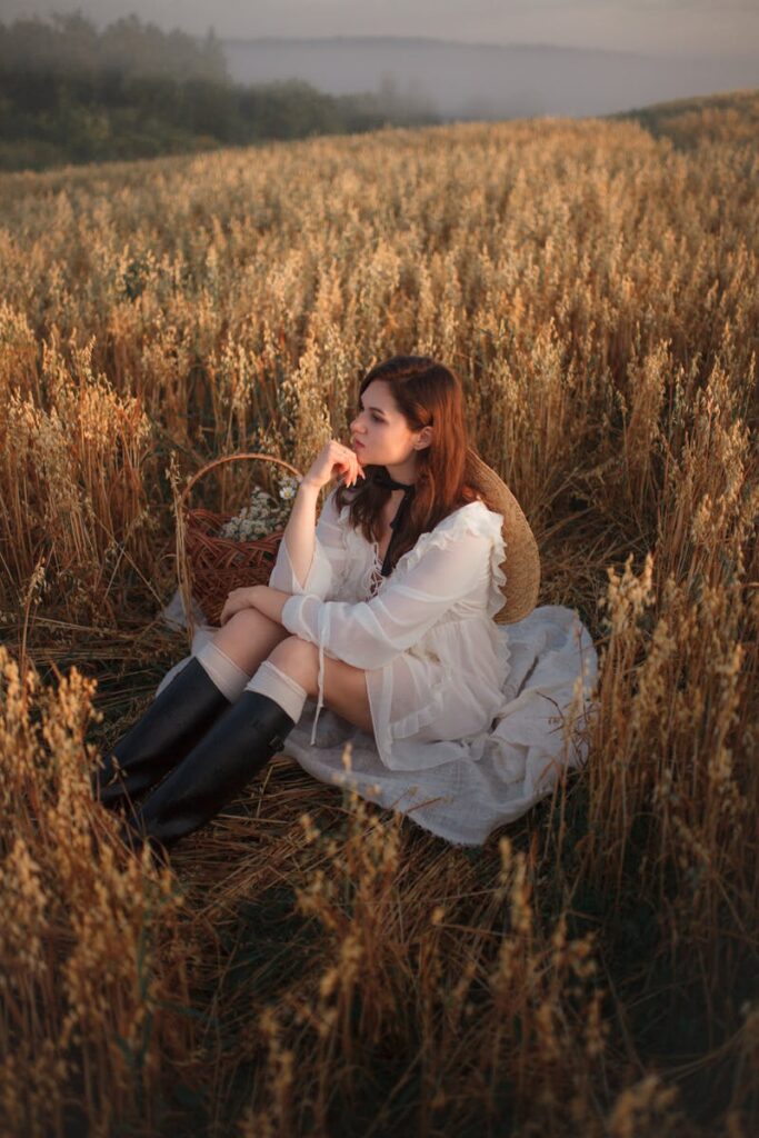 A serene portrait of a woman in a white dress sitting in a golden field during sunset.