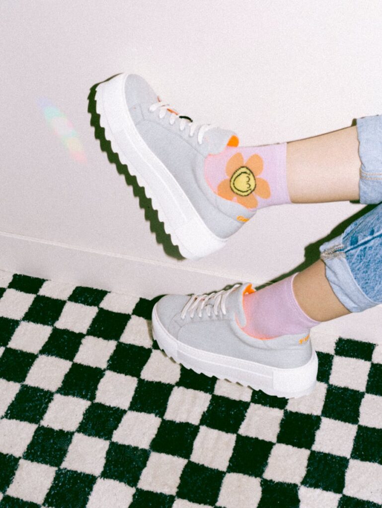 Person wearing floral socks and chunky sneakers on a checkered carpet. Casual comfort and style.