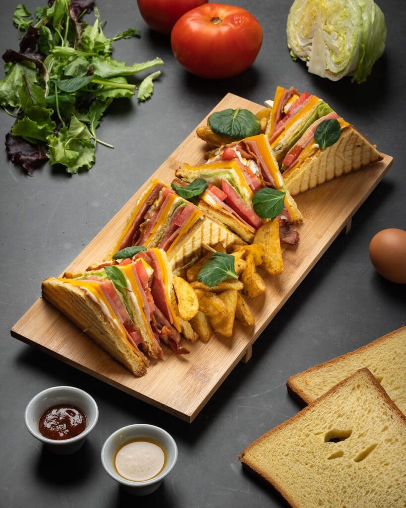 Gourmet club sandwich with fresh vegetables and fries on a wooden platter.