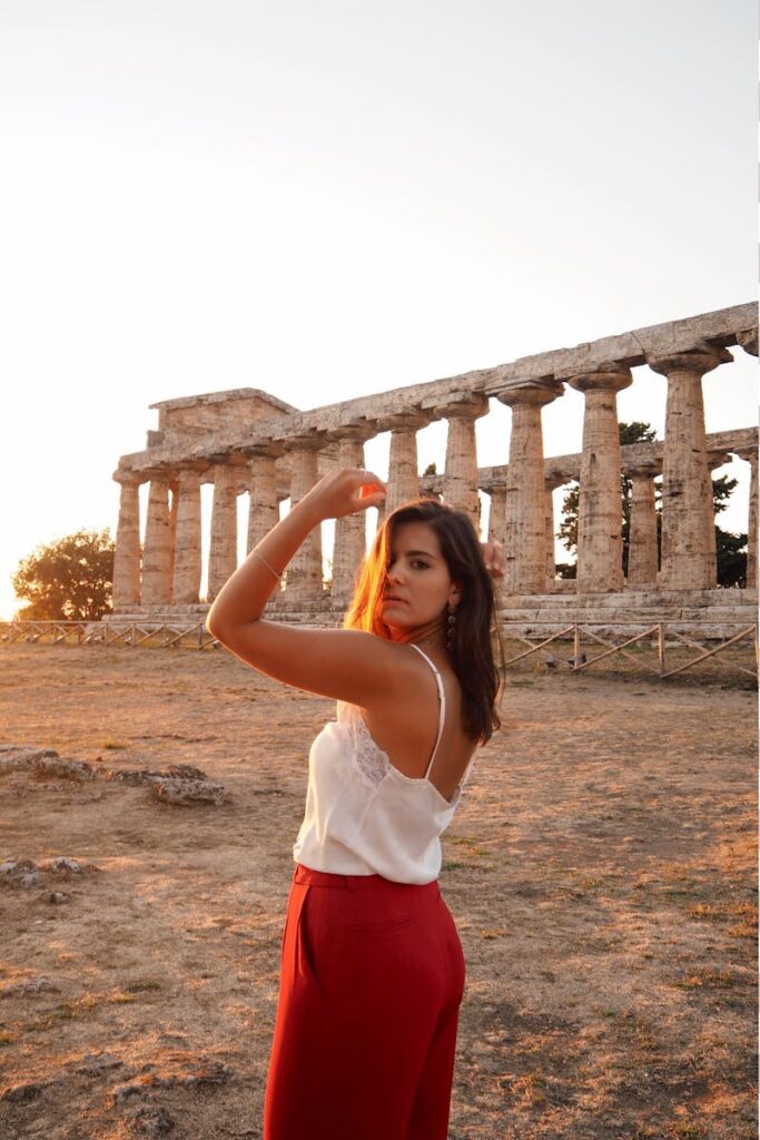 A woman poses near ancient temple ruins at sunset, marveling at historical beauty.