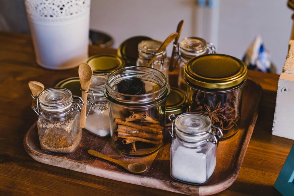An arrangement of spice jars and cinnamon sticks on a wooden tray in a cozy kitchen setting.