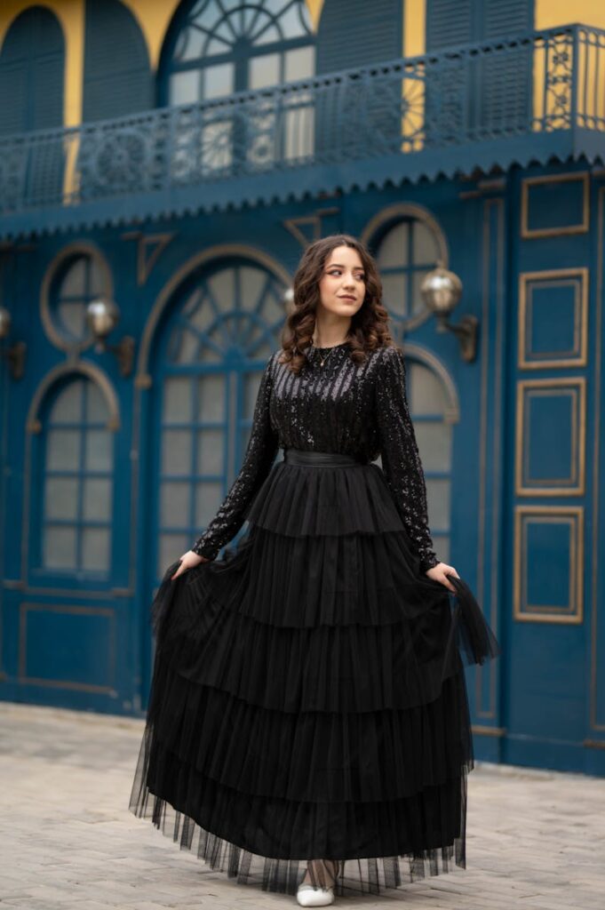 Young woman in an elegant black dress posing gracefully in front of a stylish building.