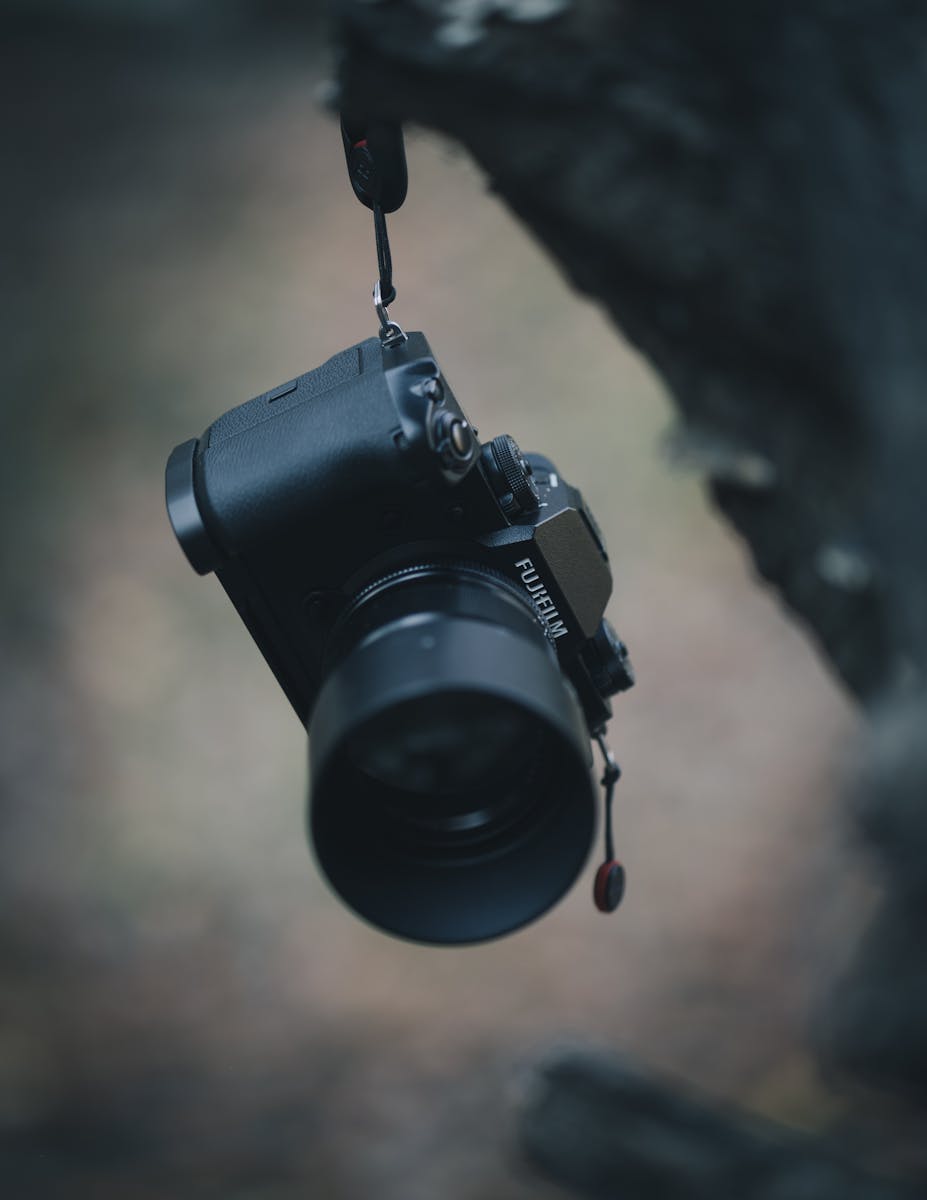 Close-up of a Fujifilm camera hanging outdoors with blurred forest background.