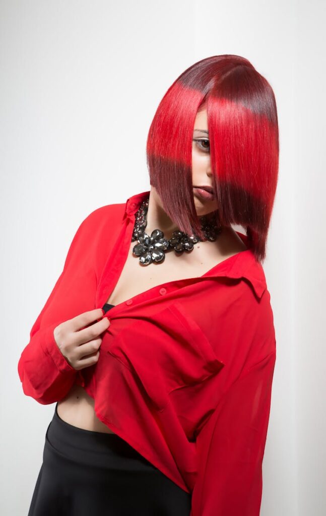 Portrait of a woman with striking red hair and necklace, showcasing bold fashion in a studio setting.