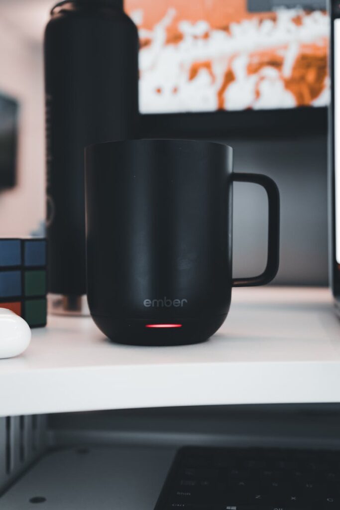 Black smart mug on a desk with Rubik's Cube and tech gadgets, perfect for tech-themed imagery.