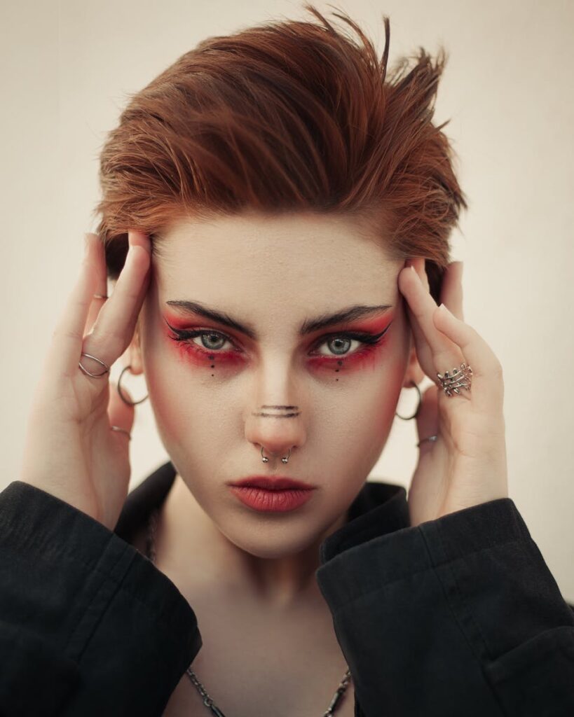 Close-up portrait of a young woman with striking makeup and short hair, embodying a modern and edgy style.