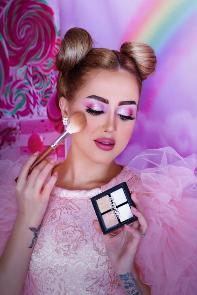 Vibrant portrait of a woman applying makeup with a pink theme and elegant hairstyle.