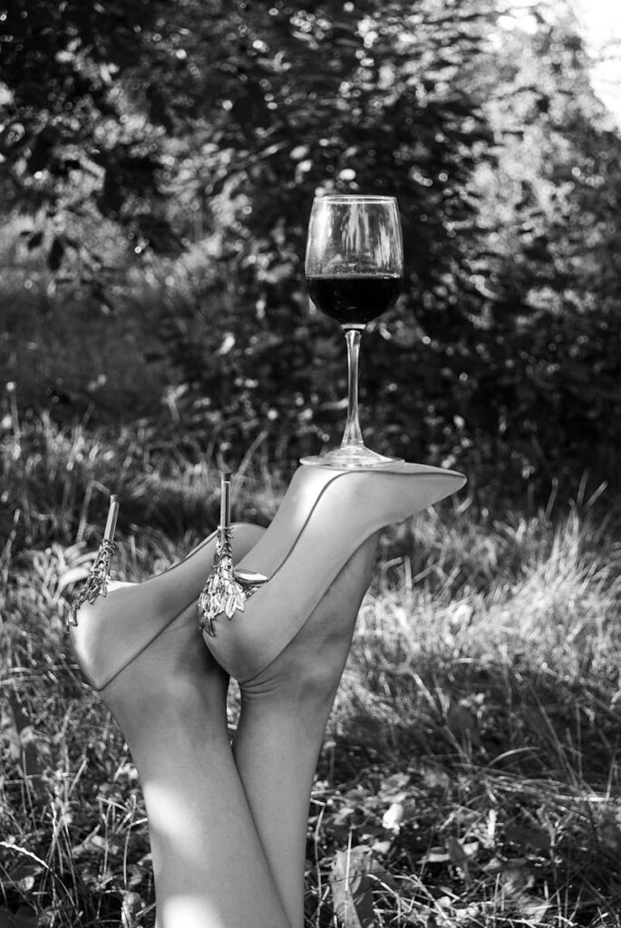 Black and white photo of stilettos balancing a wineglass outdoors.