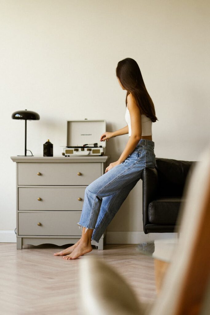 Woman in casual attire enjoying music from a vintage record player in a minimalist living room.