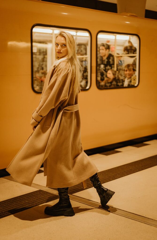 A fashionable young woman in a coat standing on a subway platform, looking back stylishly.