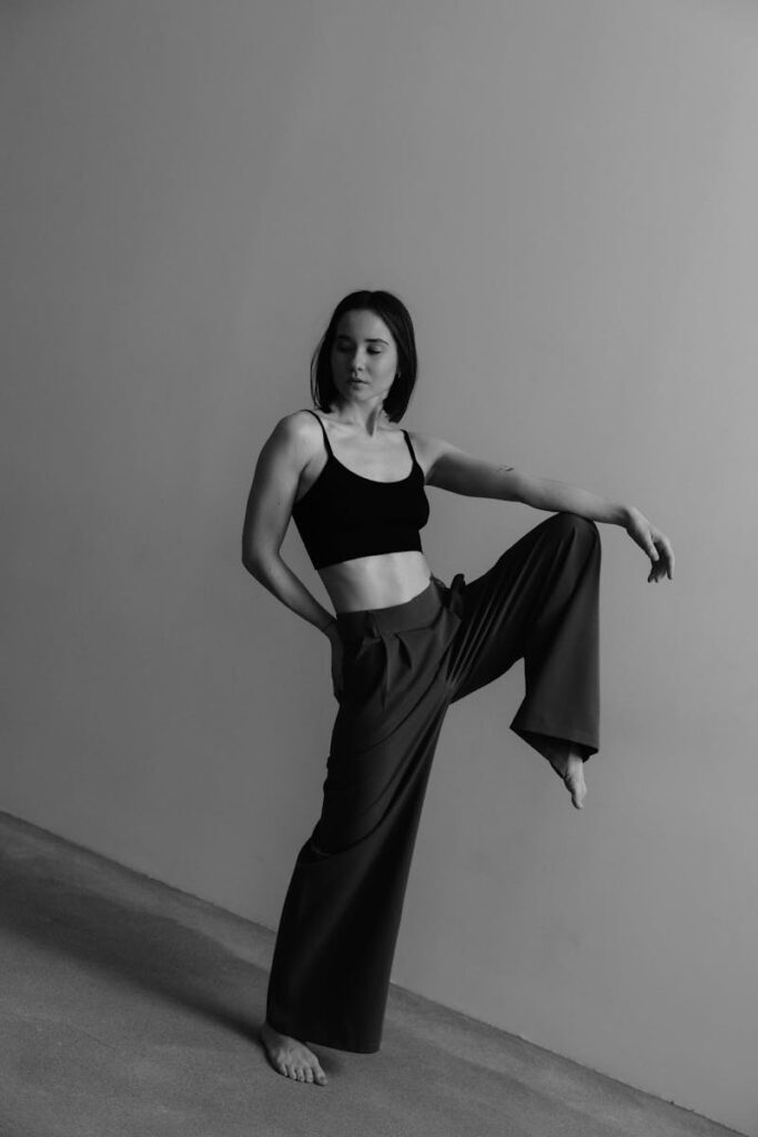 Black and white portrait of a young woman posing dramatically in a minimalist studio setting.