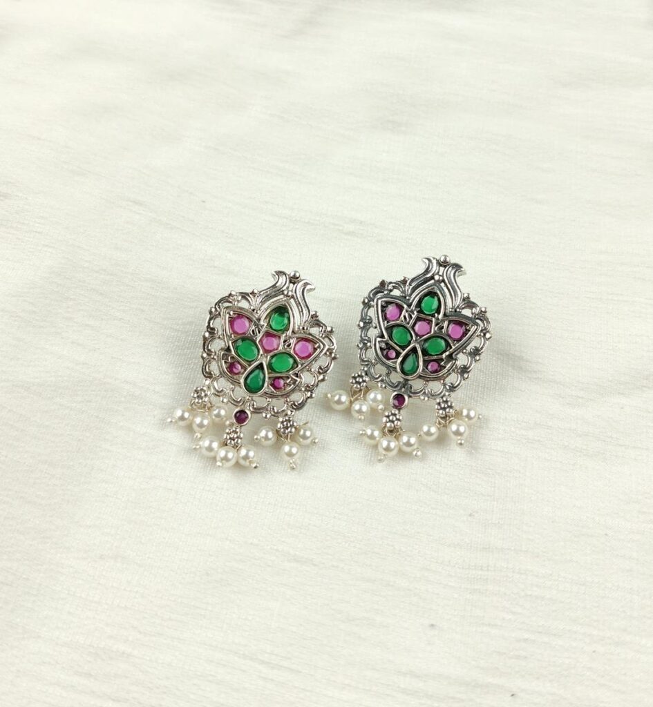 Close-up of elegant silver earrings with pearls and colorful gems on a white background.