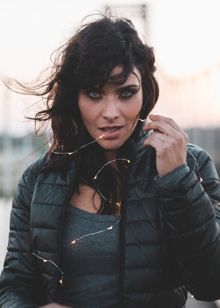 Stylish woman in black puffer jacket posing with lights in an urban setting.