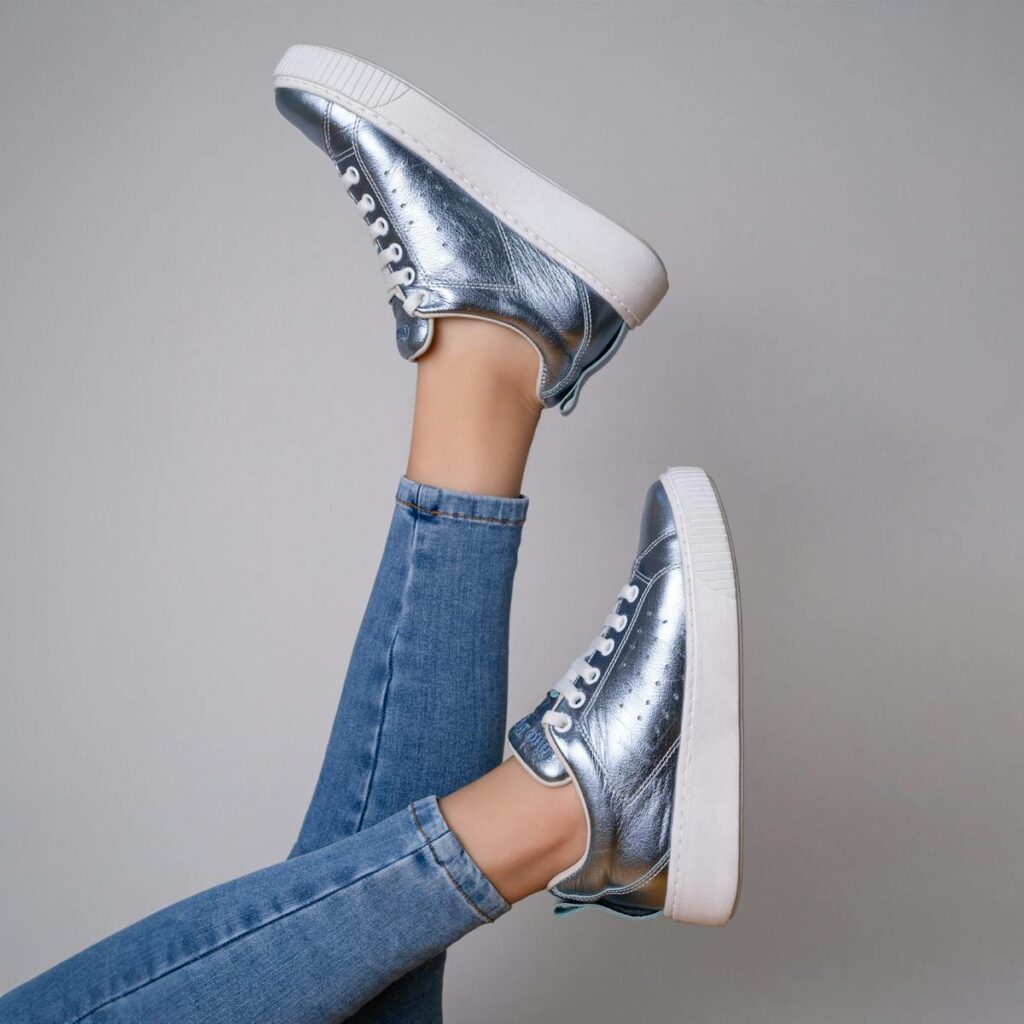 Stylish silver sneakers paired with denim jeans on a gray studio background, capturing modern fashion flair.