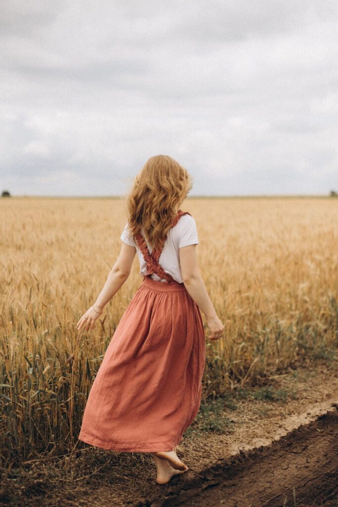 Back view of a woman walking barefoot through a golden wheat field, embodying freedom and tranquility.
