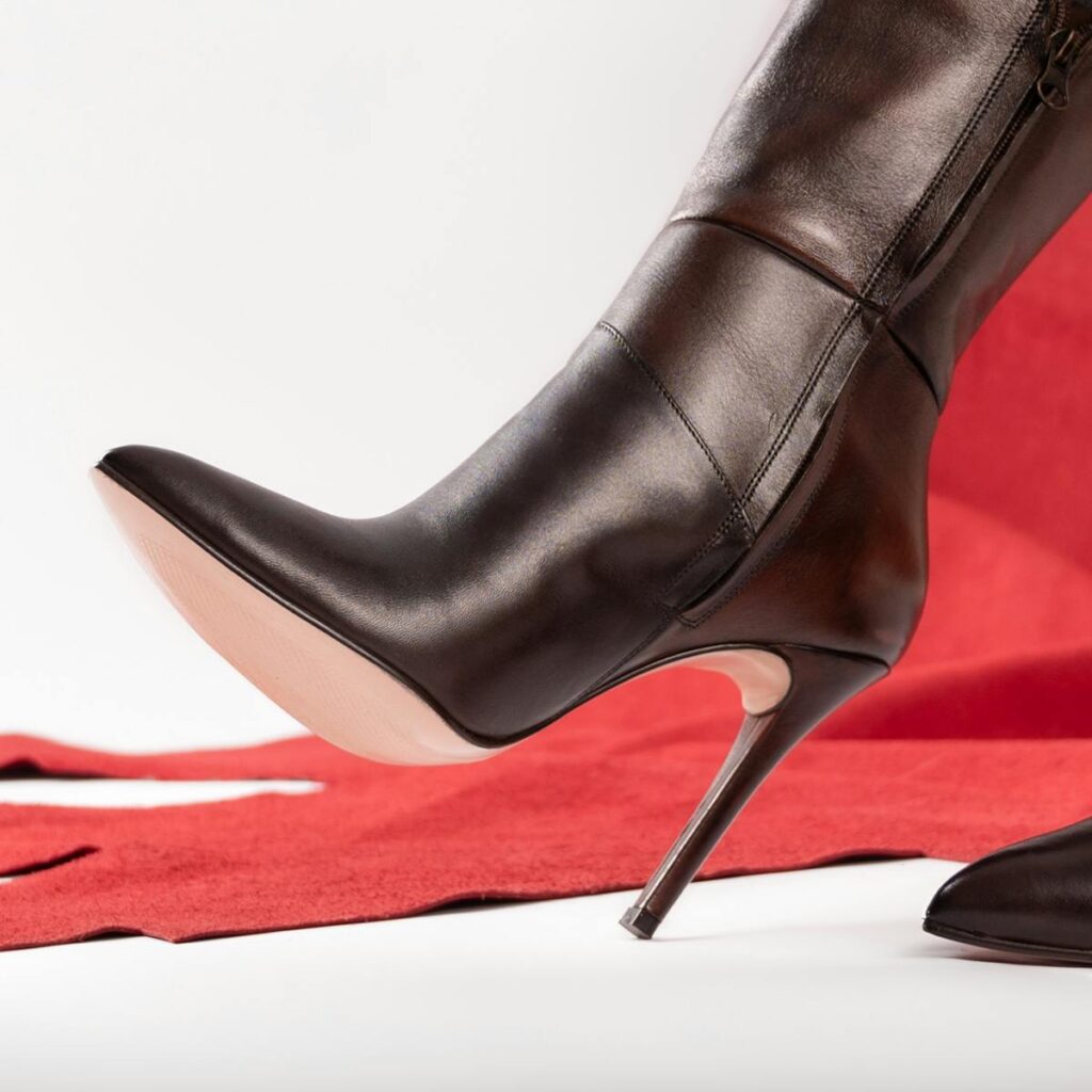 Close-up of a black leather stiletto boot on a red background, showcasing elegance and style.