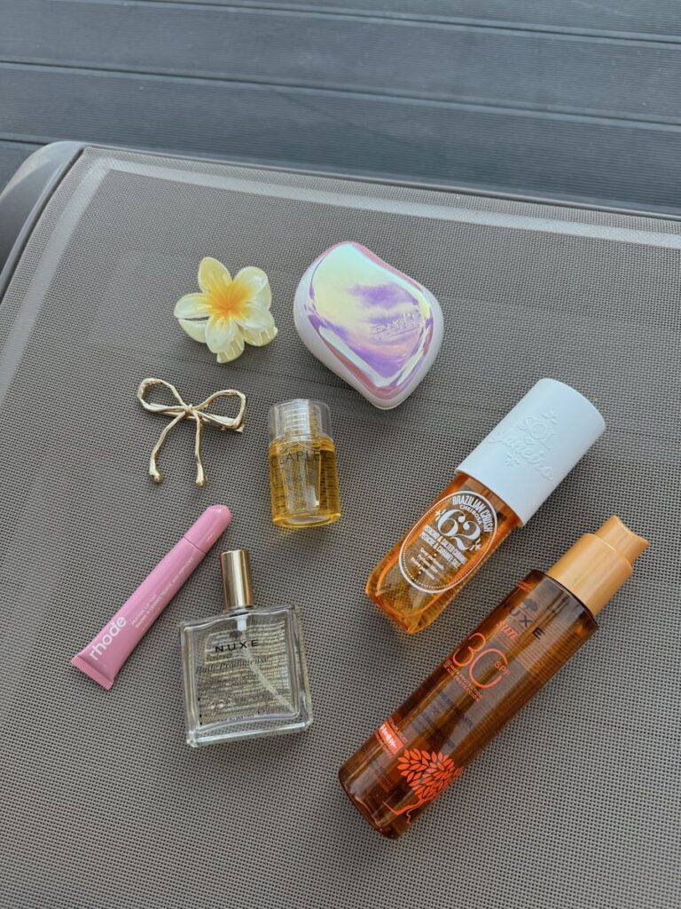 Assorted beauty products with a flower on a neutral surface.