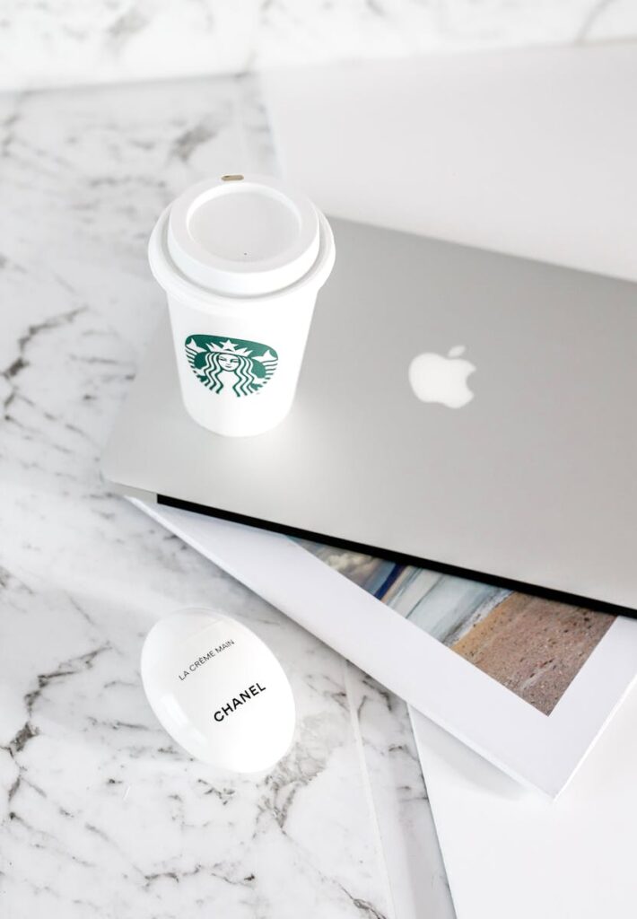 Minimalist workspace featuring a laptop, coffee cup, and brochure on marble surface.