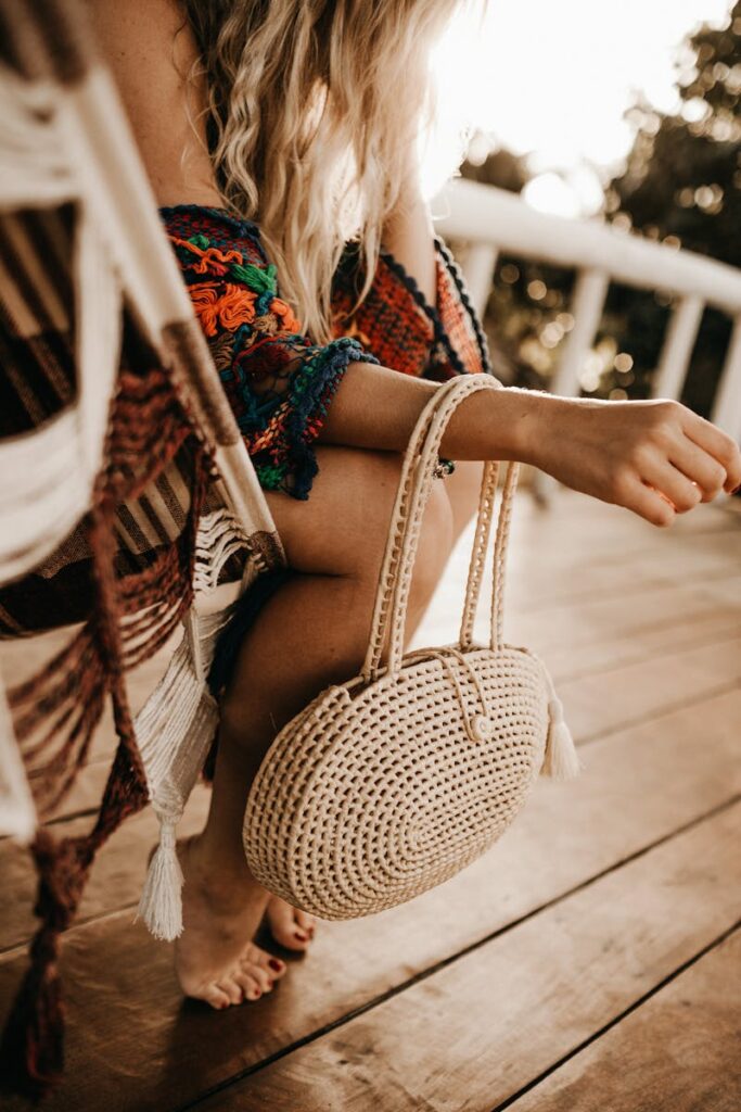 Fashionable woman in boho attire with woven bag, relaxing on sunny deck. Perfect for summer vibes.