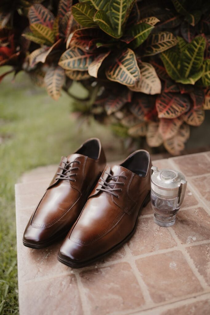 Stylish brown leather shoes paired with cologne on a tiled surface, set in an outdoor garden.