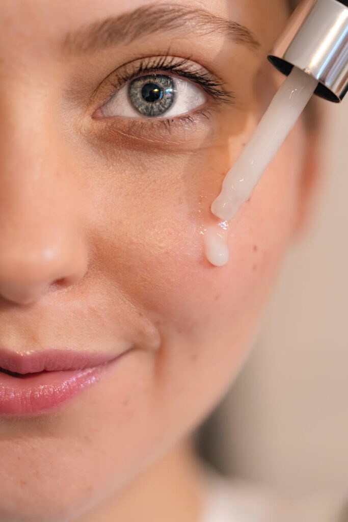 Close-up of a woman's face with serum dropper applying skincare product for healthy skin.