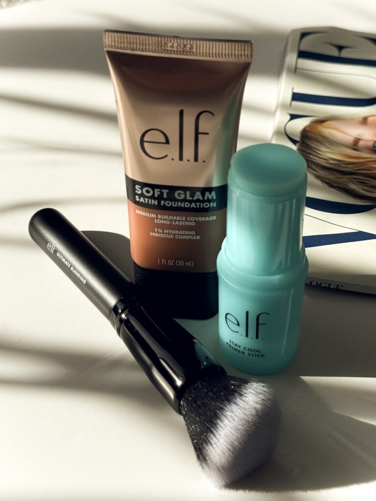 E.L.F. makeup set featuring foundation, primer stick, and brush on a magazine under sunlight.