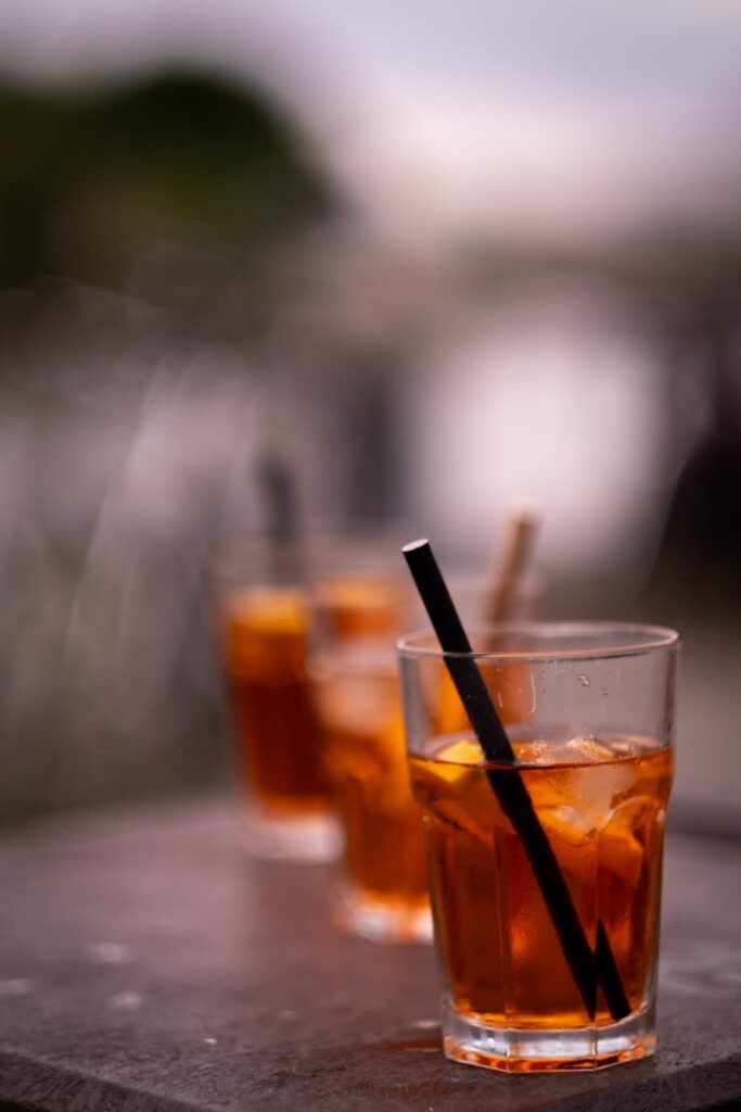 Three iced tea glasses with black straws on a wooden table outdoors, blurred background.