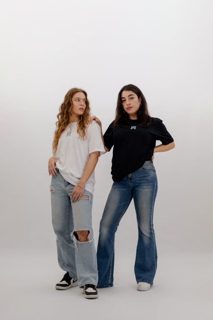 Two women pose in casual attire, embodying contemporary fashion in a studio setting.