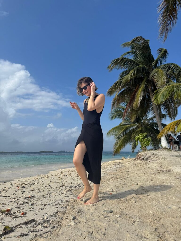 A woman strolls along a palm-lined beach in Guna Yala, Panama, under a bright blue sky.