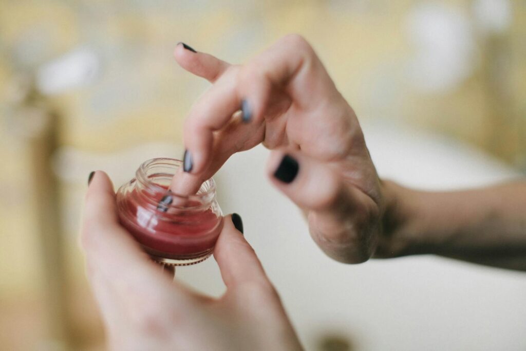 Close-up of a woman applying balm from a glass jar, focusing on skincare aesthetics.