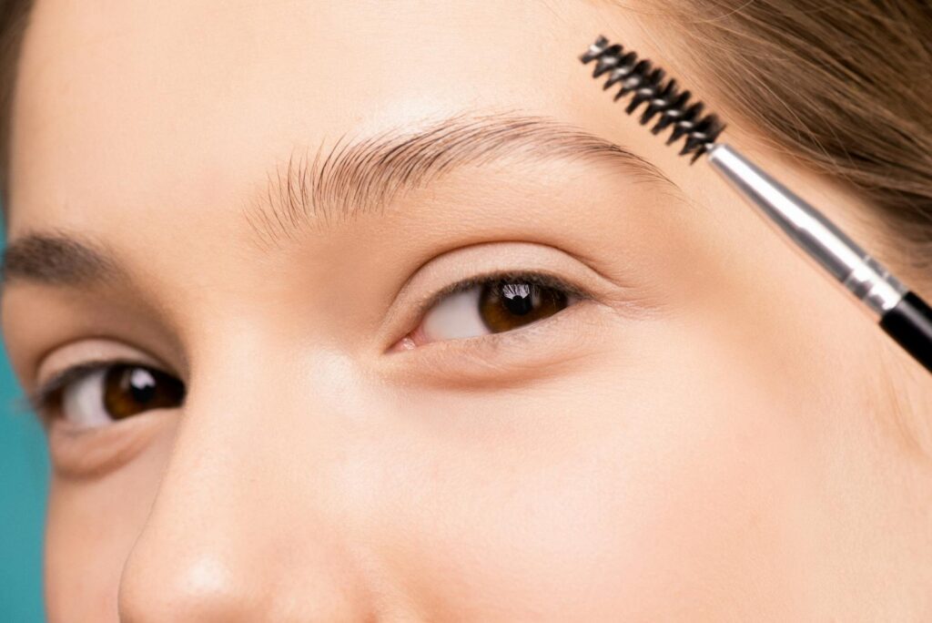 Close-up of a woman applying makeup with an eyebrow brush, highlighting natural beauty.
