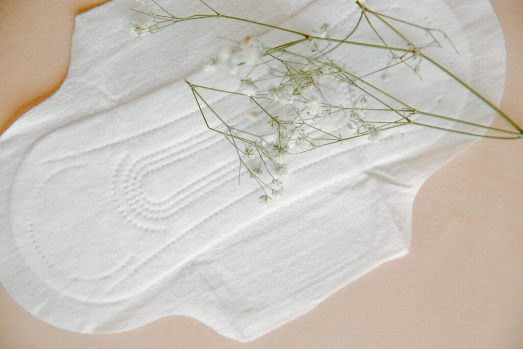 Elegant composition of a white sanitary pad with delicate gypsophila flowers, set on a neutral background.