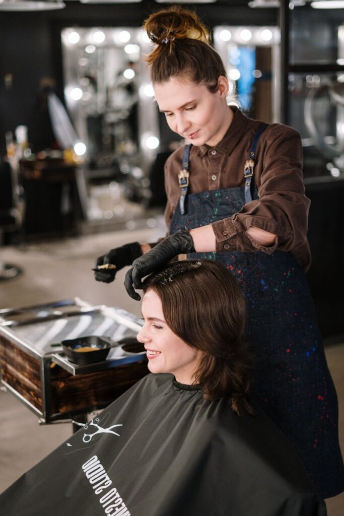 Hairdresser applying color to woman's hair in a modern salon, capturing a lively professional atmosphere.