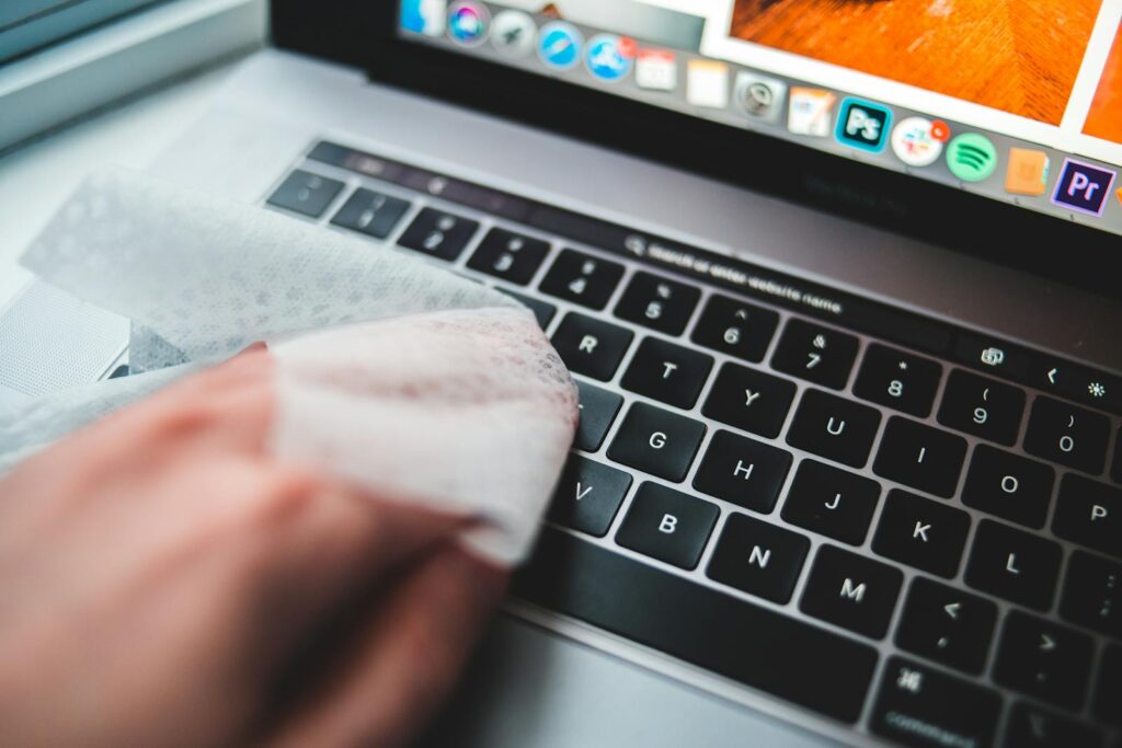 Person cleaning a laptop keyboard using disinfectant wipes for hygiene.
