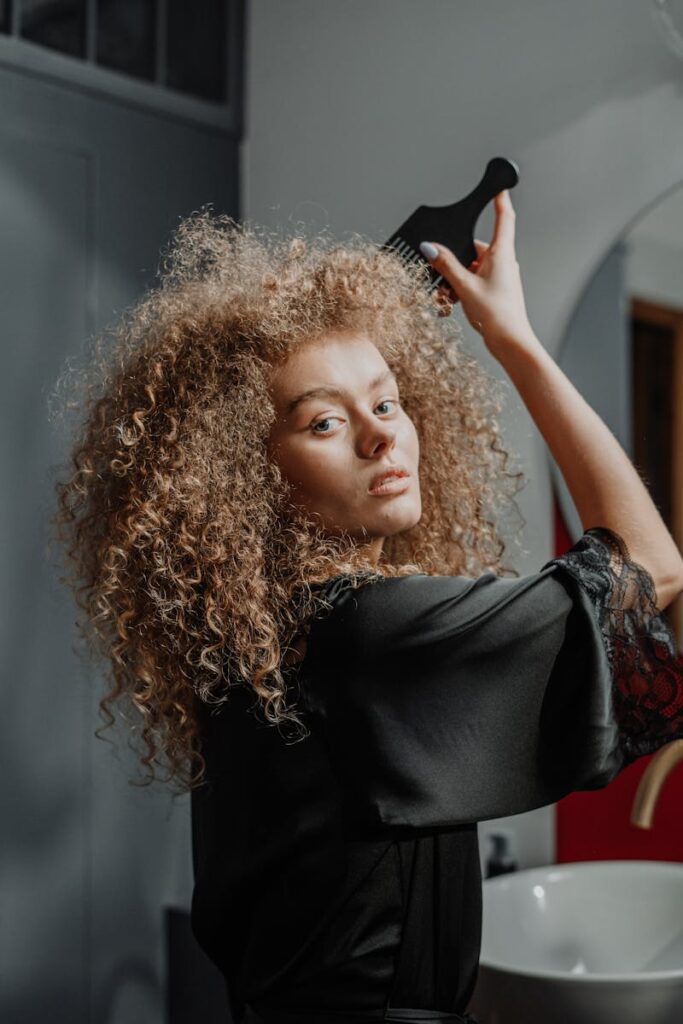 Portrait of a young woman with curly hair using a comb indoors, showcasing beauty and self-care.