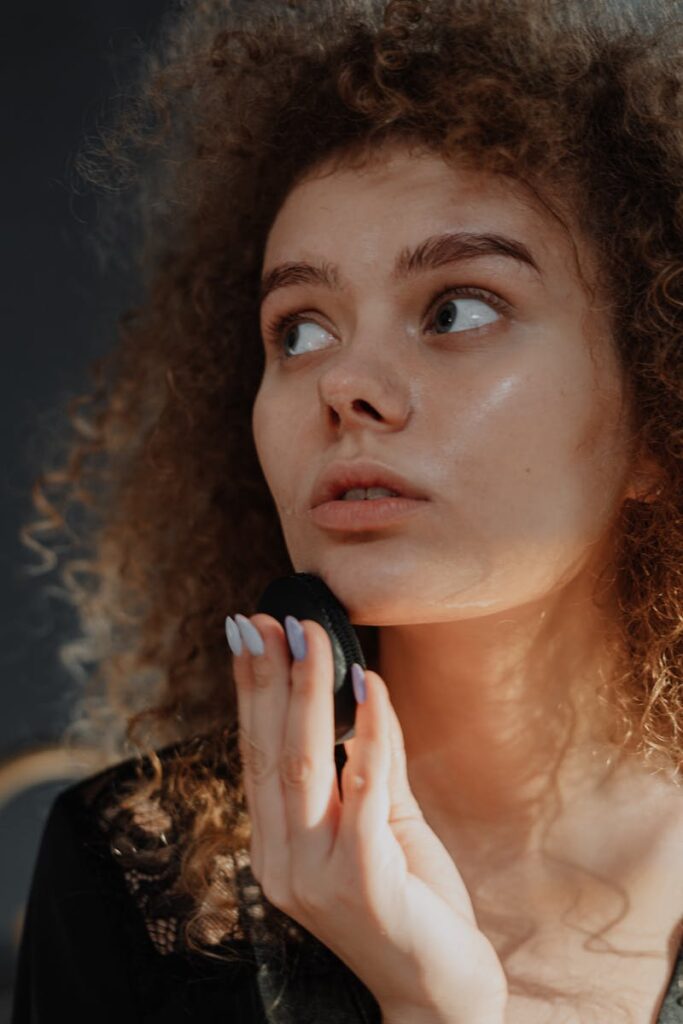 Portrait of a young woman with natural curly hair applying beauty product, highlighting skincare and self-care.