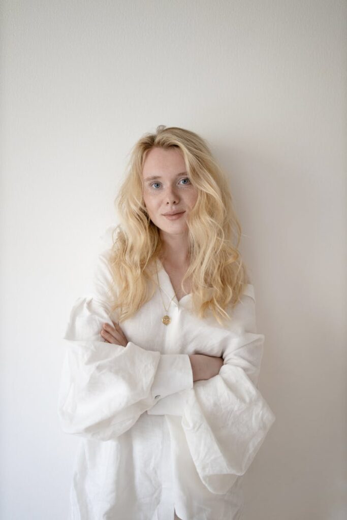 Graceful portrait of a smiling blonde woman wearing a white shirt against a plain backdrop.