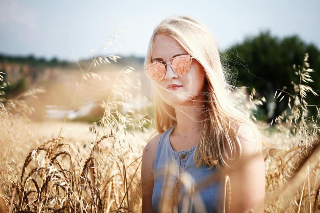 Blonde woman in sunglasses standing in a sunny wheat field.