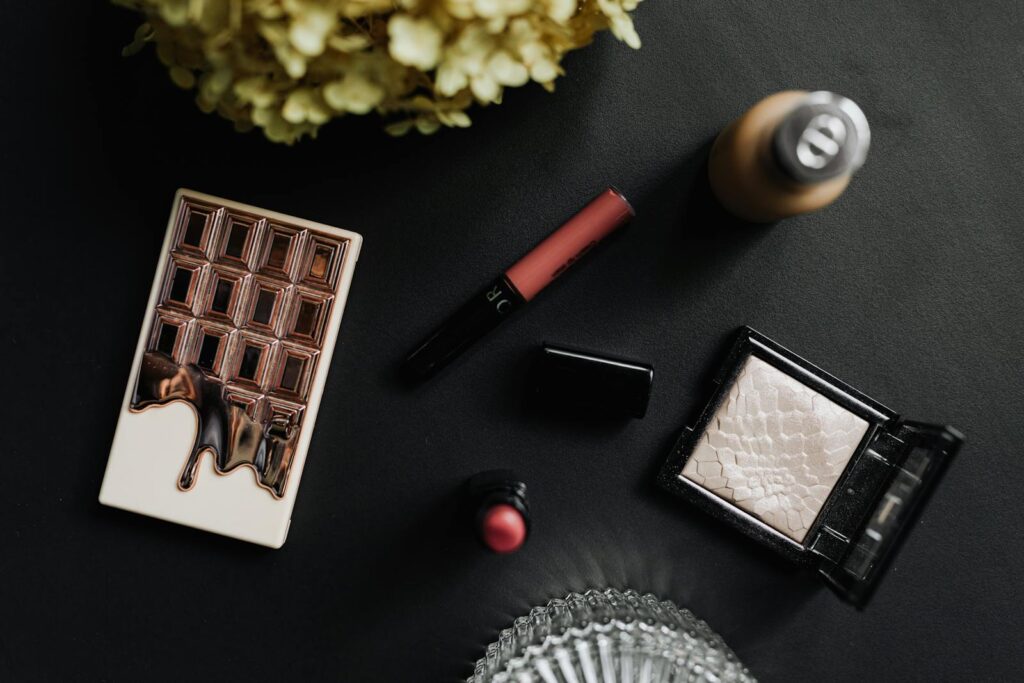 Flat lay of luxury makeup items on a black table with cosmetics and accessories.