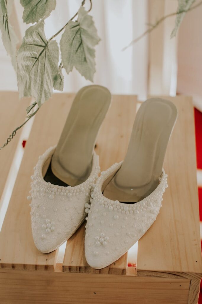 Close-up of stylish white beaded mule shoes on a wooden surface, perfect for elegant occasions.