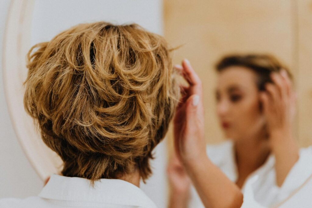 Back view of a woman styling her short hair while looking in the mirror.