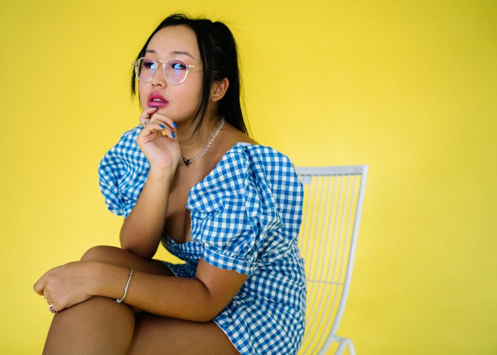 Fashionable woman posing indoors, wearing blue gingham dress against a yellow background. Studio shoot.