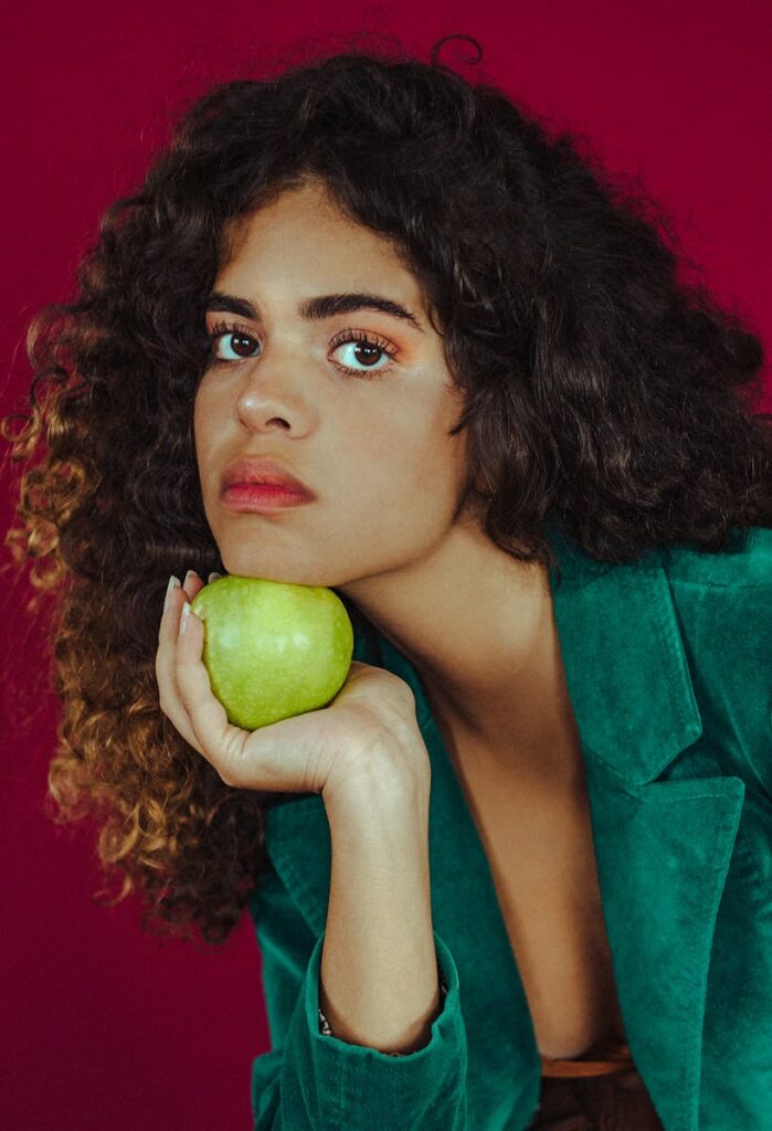 A striking portrait of a woman holding a green apple against a bold background.