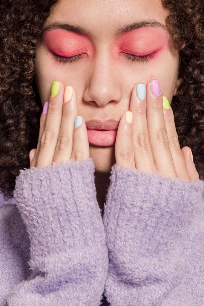 Close-up portrait of a woman with vibrant eyeshadow and pastel manicure, evoking a sense of contemporary style.